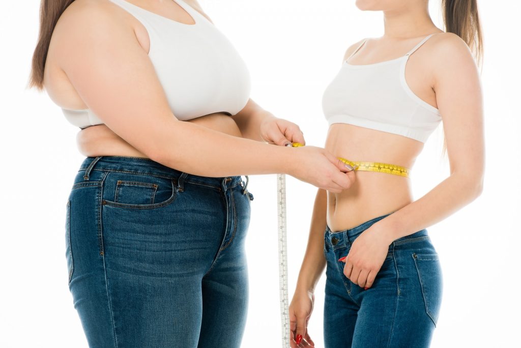 cropped view of overweight woman measuring waist of slim woman isolated on white