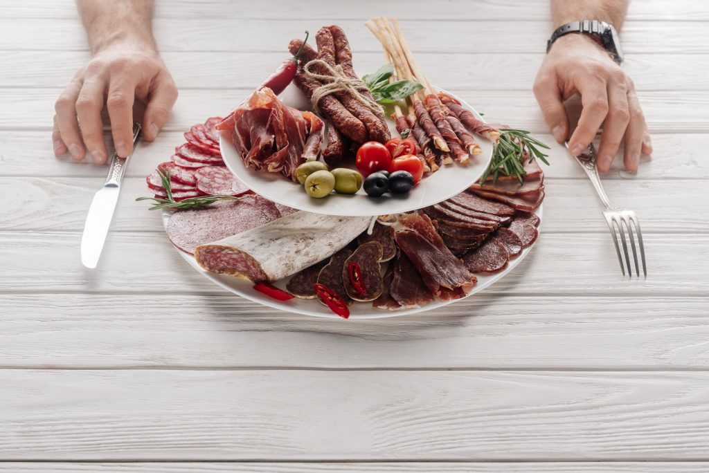 partial view of man at white wooden tabletop with various meat snacks